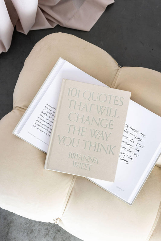 Book '101 Quotes That Will Change The Way You Think' by Brianna Wiest on beige cushion, open book beneath. Come see us at Awaken, Franklin, Tennessee