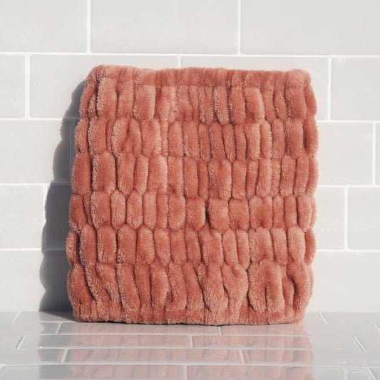 Soft textured plush rose-colored cushion against white tiled wall. Come see us at Awaken, Franklin, Tennessee