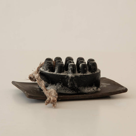 Black massage soap bar with rope on brown dish with foam bubbles. Come see us at Awaken, Franklin, Tennessee.