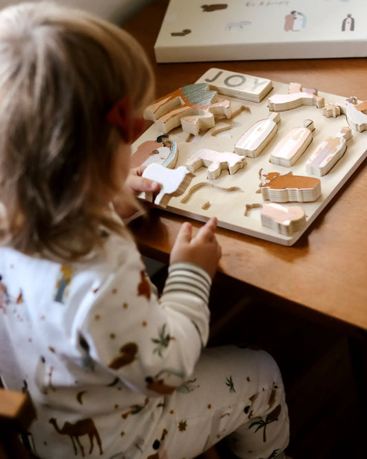 Child playing with wooden nativity puzzle on table, wearing animal print pajamas. Come see us at Awaken, Franklin, Tennessee