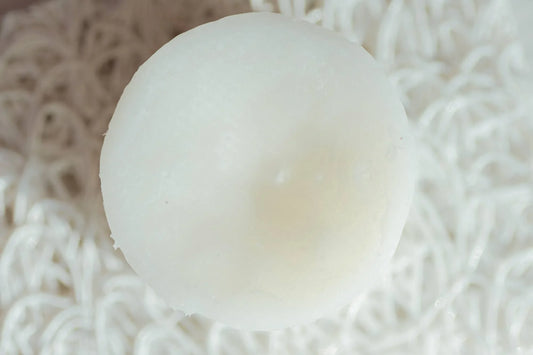Close-up of a white tealight candle on white shredded paper background, minimal decor. Come see us at Awaken, Franklin, Tennessee