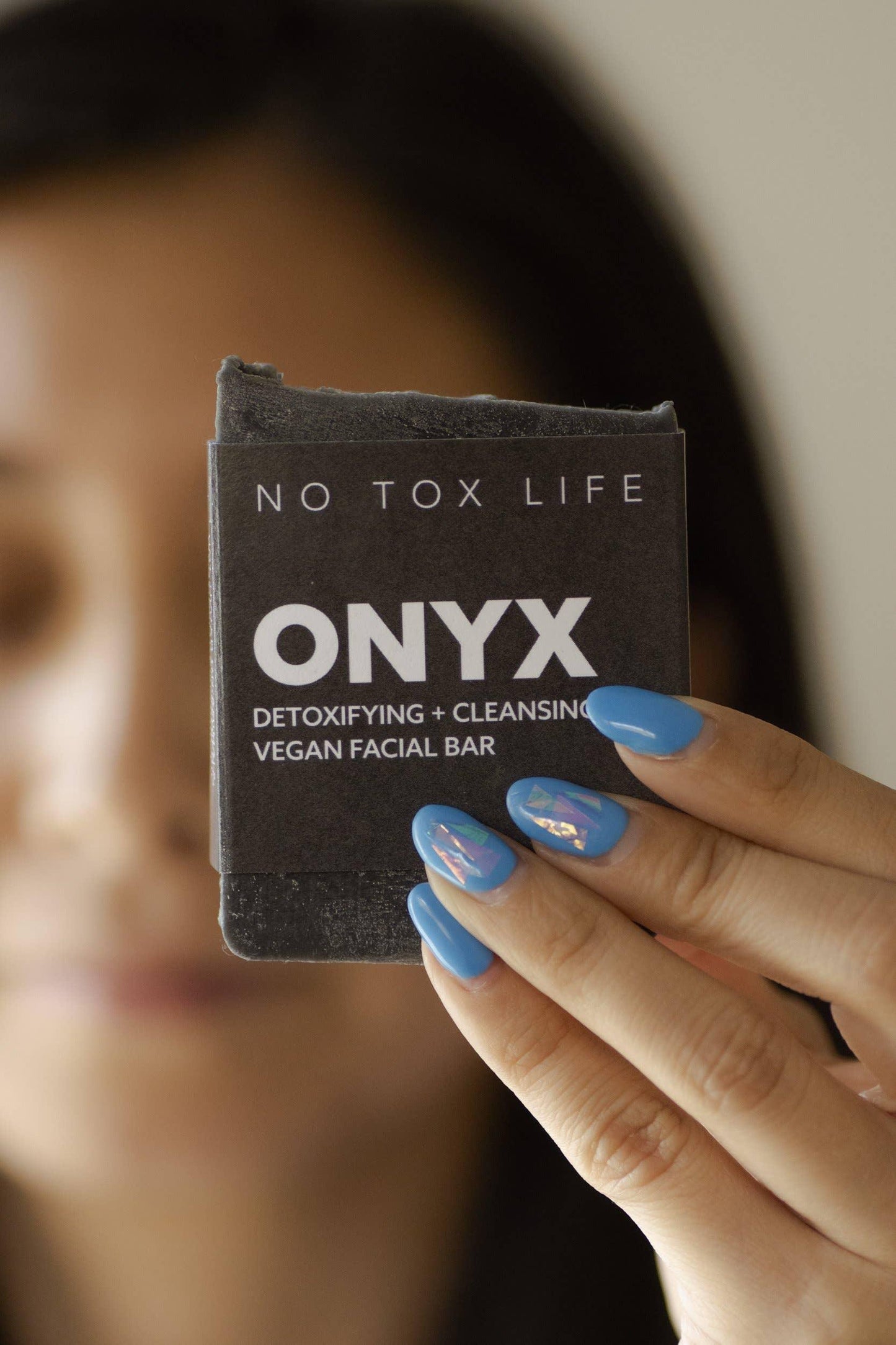 Hand with blue nails holding ONYX detoxifying vegan facial bar; Come see us at Awaken, Franklin, Tennessee