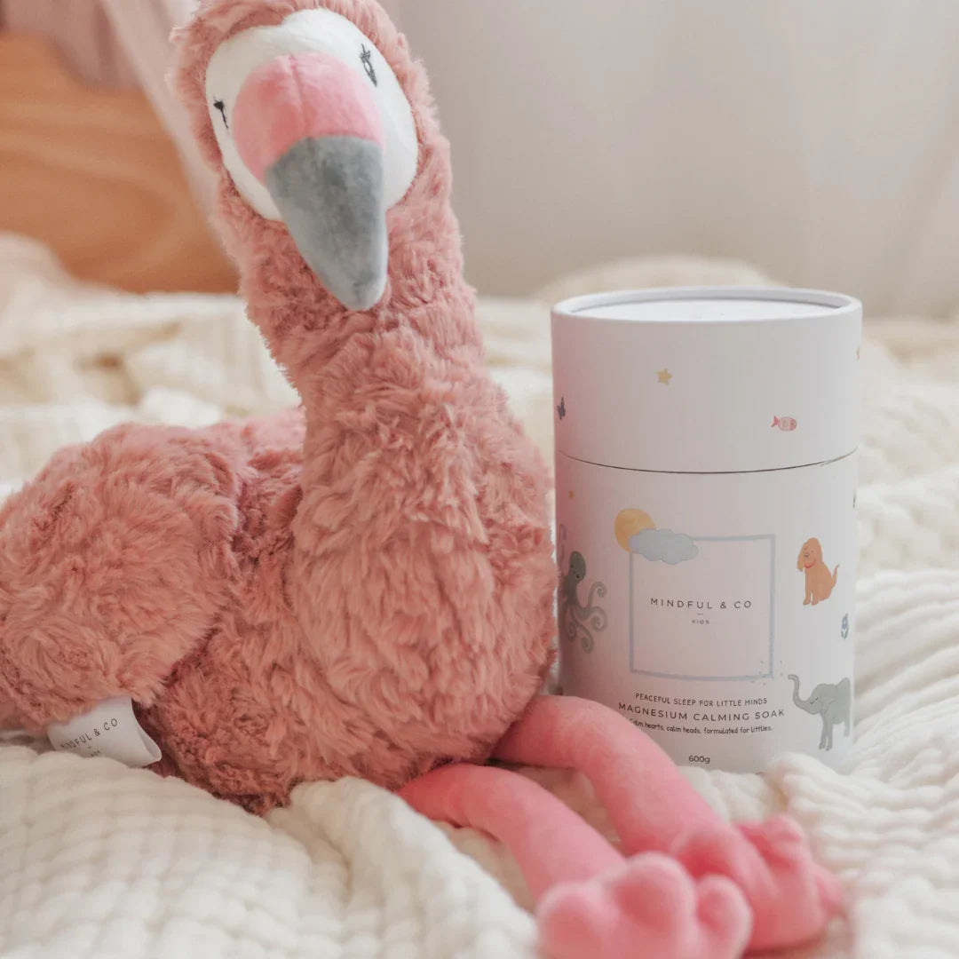 Soft pink flamingo plush toy beside Mindful & Co Kids magnesium calming soak on cozy white blanket. Come see us at Awaken, Franklin, Tennessee