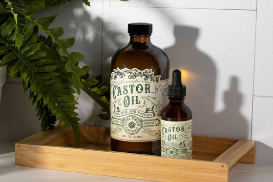 Two amber bottles of cold pressed castor oil on a wooden tray with green fern leaves, Come see us at Awaken, Franklin, Tennessee