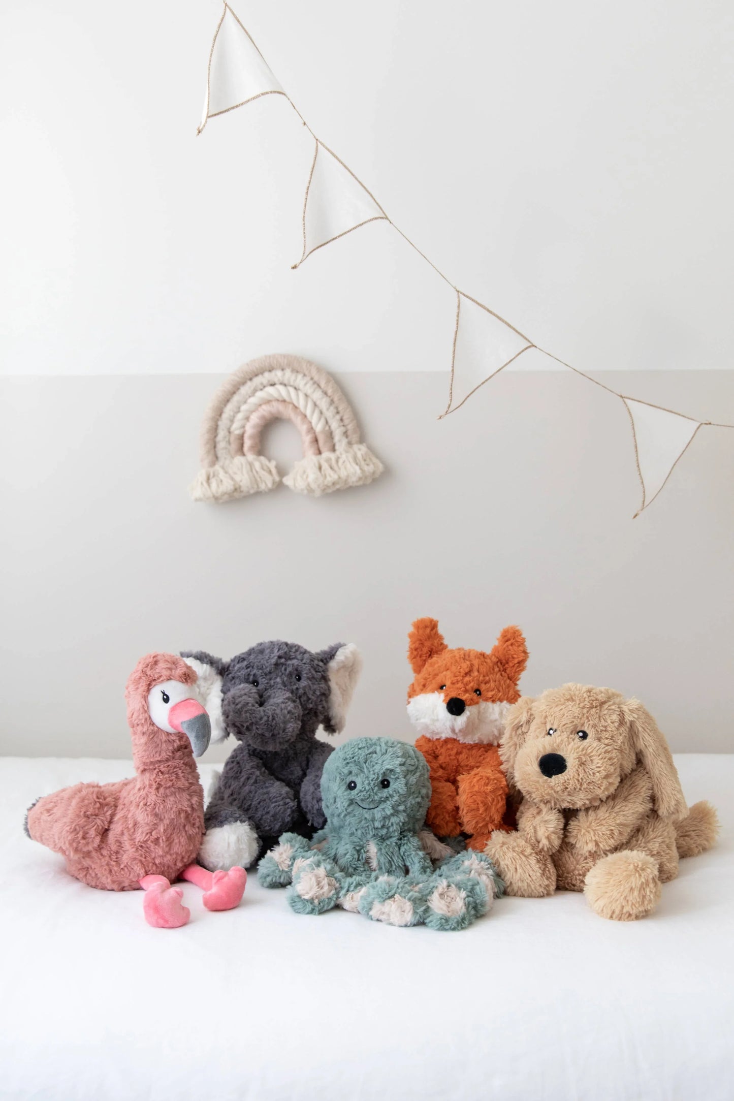 Plush animal toys including flamingo, elephant, octopus, fox, and dog on a white bed with wall decor. Come see us at Awaken, Franklin, Tennessee