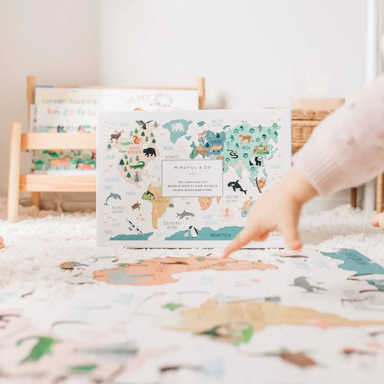 Child assembling colorful world map floor puzzle on carpet with illustrated animals. Come see us at Awaken, Franklin, Tennessee