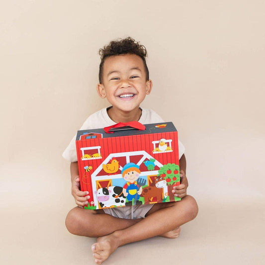 Smiling child sitting cross-legged holding colorful farm playset box, Come see us at Awaken, Franklin, Tennessee