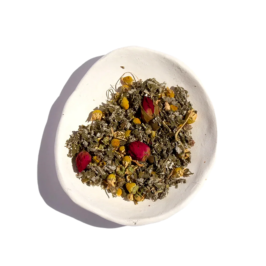 White ceramic bowl with dried herbal tea blend including chamomile and red rosebuds, bright background. Come see us at Awaken, Franklin, Tennessee