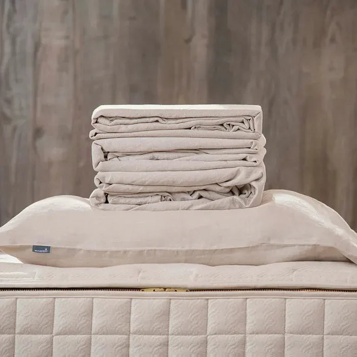 Stack of beige linen bedding including pillow and quilt on patterned mattress, Come see us at Awaken, Franklin, Tennessee