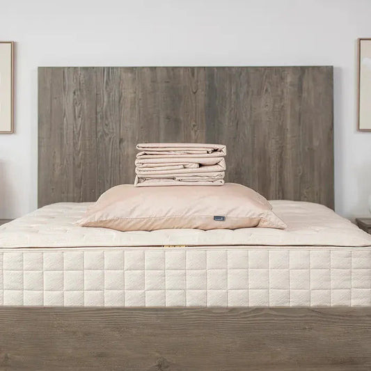 Beige bedding set including pillow and folded sheets on mattress with wooden headboard in bedroom. Come see us at Awaken, Franklin, Tennessee