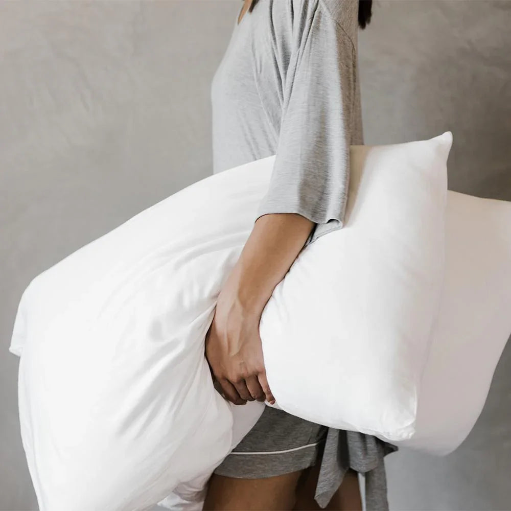Person holding a large white pillow wearing gray loungewear against a neutral wall. Come see us at Awaken, Franklin, Tennessee