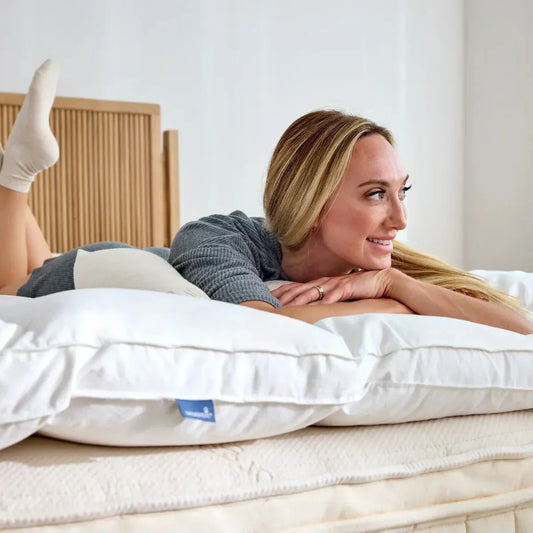 Smiling woman lying on white pillow and mattress in bright bedroom, Come see us at Awaken, Franklin, Tennessee
