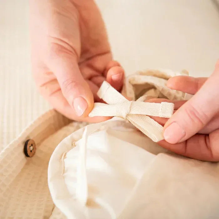 Hands tying a beige cotton garment string on textured fabric with button, close-up. Come see us at Awaken, Franklin, Tennessee