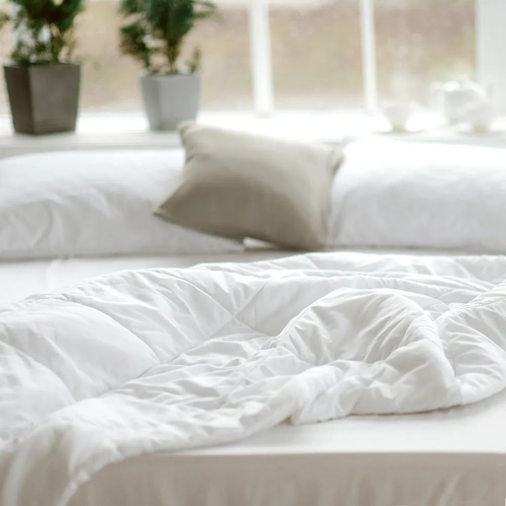 Cozy white comforter and pillows on bed with potted plants, Come see us at Awaken, Franklin, Tennessee