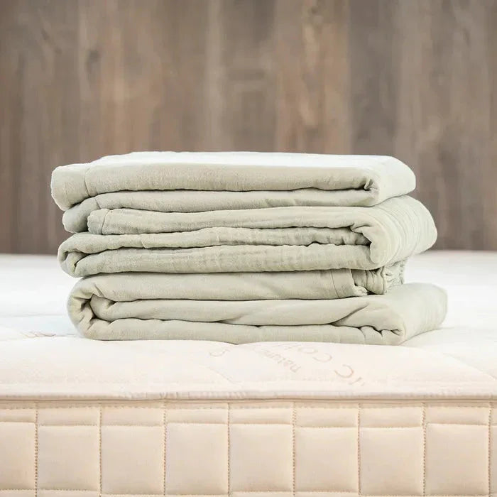 Folded light green bedding on beige mattress with wood wall background. Come see us at Awaken, Franklin, Tennessee
