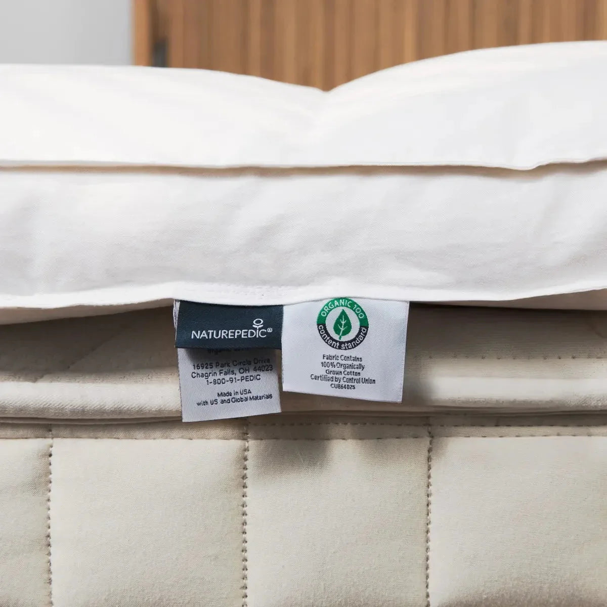 Naturepedic mattress tags showing 100% organic cotton fabric certification, quilted beige mattress in background. Come see us at Awaken, Franklin, Tennessee