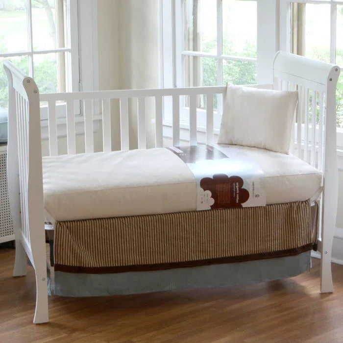 White baby crib with beige bedding and pillow in bright room with wooden floor, Come see us at Awaken, Franklin, Tennessee