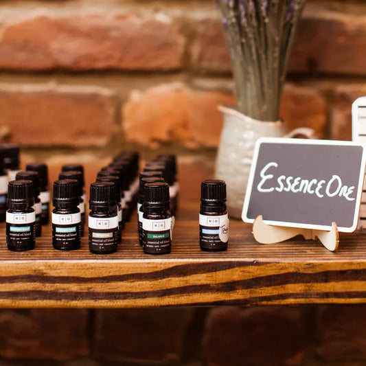 Essence One essential oil blends displayed on wooden shelf with brick wall background. Come see us at Awaken, Franklin, Tennessee