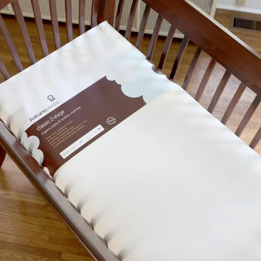 Organic Naturepedic classic 2-stage baby mattress inside wooden crib on hardwood floor. Come see us at Awaken, Franklin, Tennessee