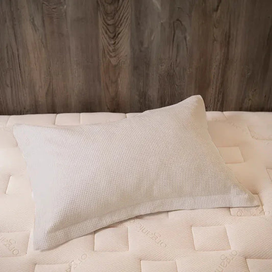 White textured pillow on an organic mattress with wood backdrop, soft bedding. Come see us at Awaken, Franklin, Tennessee