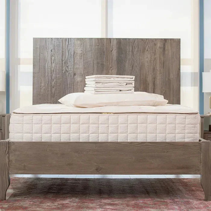 Modern wooden bed frame with white mattress, pillows, and folded sheets in bright room. Come see us at Awaken, Franklin, Tennessee