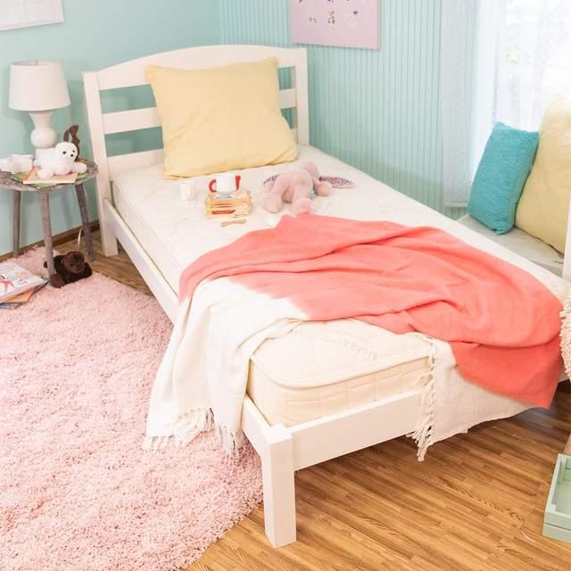 White wooden single bed with pink and white blankets in cozy pastel kid's room with toys and cushions. Come see us at Awaken, Franklin, Tennessee
