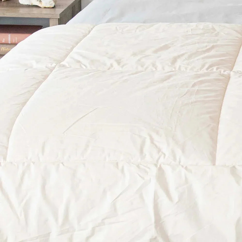 Close-up of white quilted down comforter on bed with a wooden side table and books nearby. Come see us at Awaken, Franklin, Tennessee