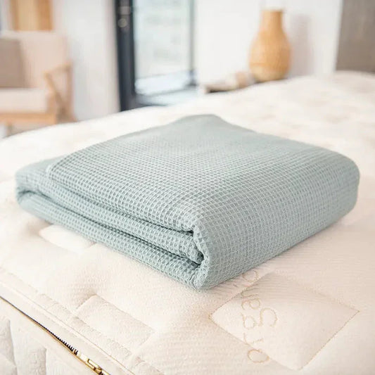 Folded light blue textured blanket on a white mattress in cozy bedroom setting. Come see us at Awaken, Franklin, Tennessee