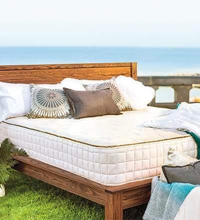 Wooden bed with white mattress and decorative pillows on seaside lawn. Come see us at Awaken, Franklin, Tennessee