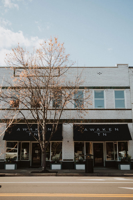 White brick storefront with black awnings reading Awaken TN and leafless tree in front Come see us at Awaken, Franklin, Tennessee