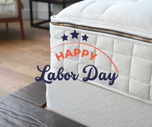 Close-up of a white mattress with Happy Labor Day text and stars overlaid, wooden floor background, Come see us at Awaken, Franklin, Tennessee