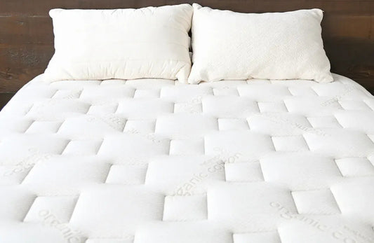 Close-up of a white organic cotton mattress with two white pillows against a wooden headboard. Come see us at Awaken, Franklin, Tennessee