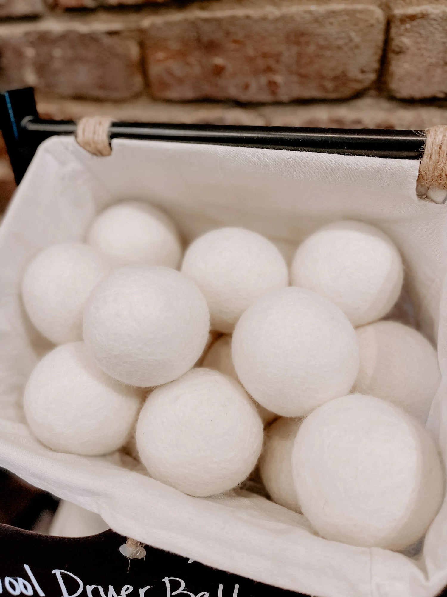 White wool dryer balls in a fabric basket against a brick wall, Come see us at Awaken, Franklin, Tennessee