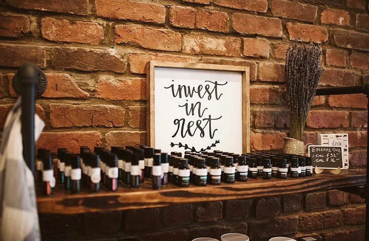 Essential oils on wooden shelf, 'invest in rest' sign, rustic brick wall, Come see us at Awaken, Franklin, Tennessee