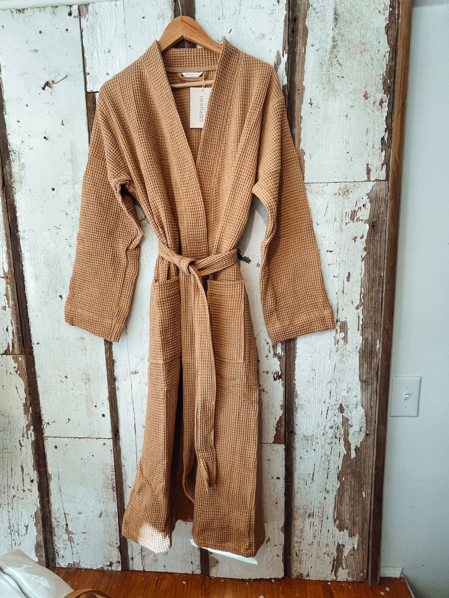 Tan waffle cotton robe on hanger, rustic wood backdrop, Come see us at Awaken, Franklin, Tennessee.