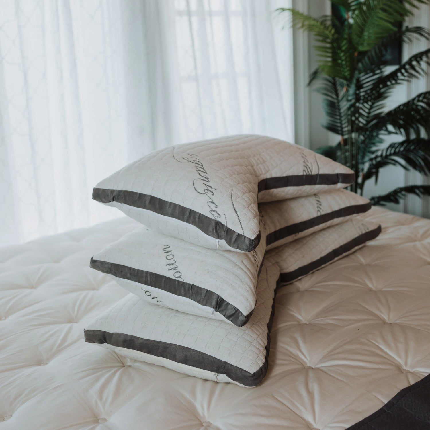 Stack of organic pillows on a bed by a window and plant, Come see us at Awaken, Franklin, Tennessee