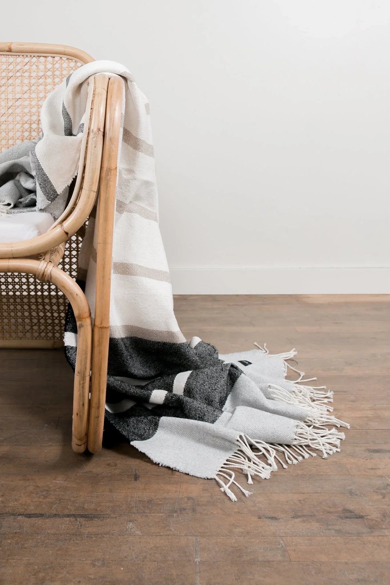 Neutral striped cotton throw blanket draped over rattan chair, Come see us at Awaken, Franklin, Tennessee