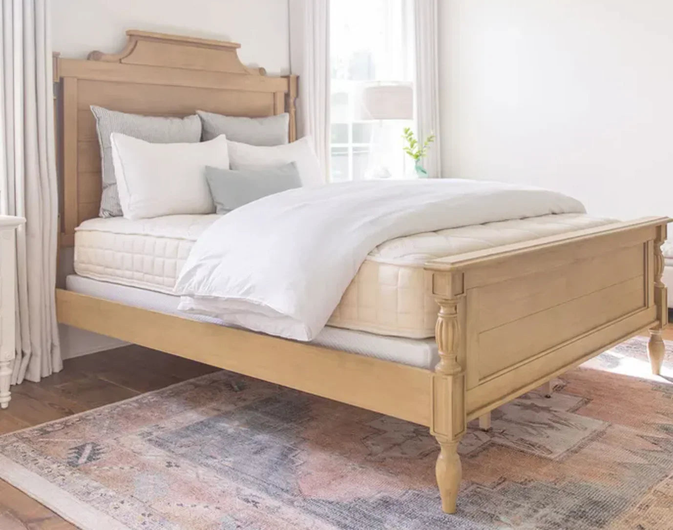 Light wood classic bedroom bed with white bedding and pillows on a patterned rug. Come see us at Awaken, Franklin, Tennessee
