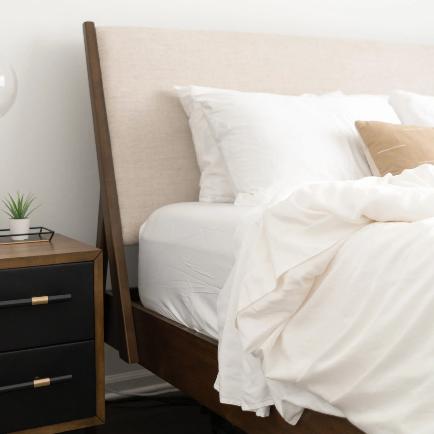 Modern bedroom with white sheet set, beige headboard, wood nightstand, Come see us at Awaken, Franklin, Tennessee