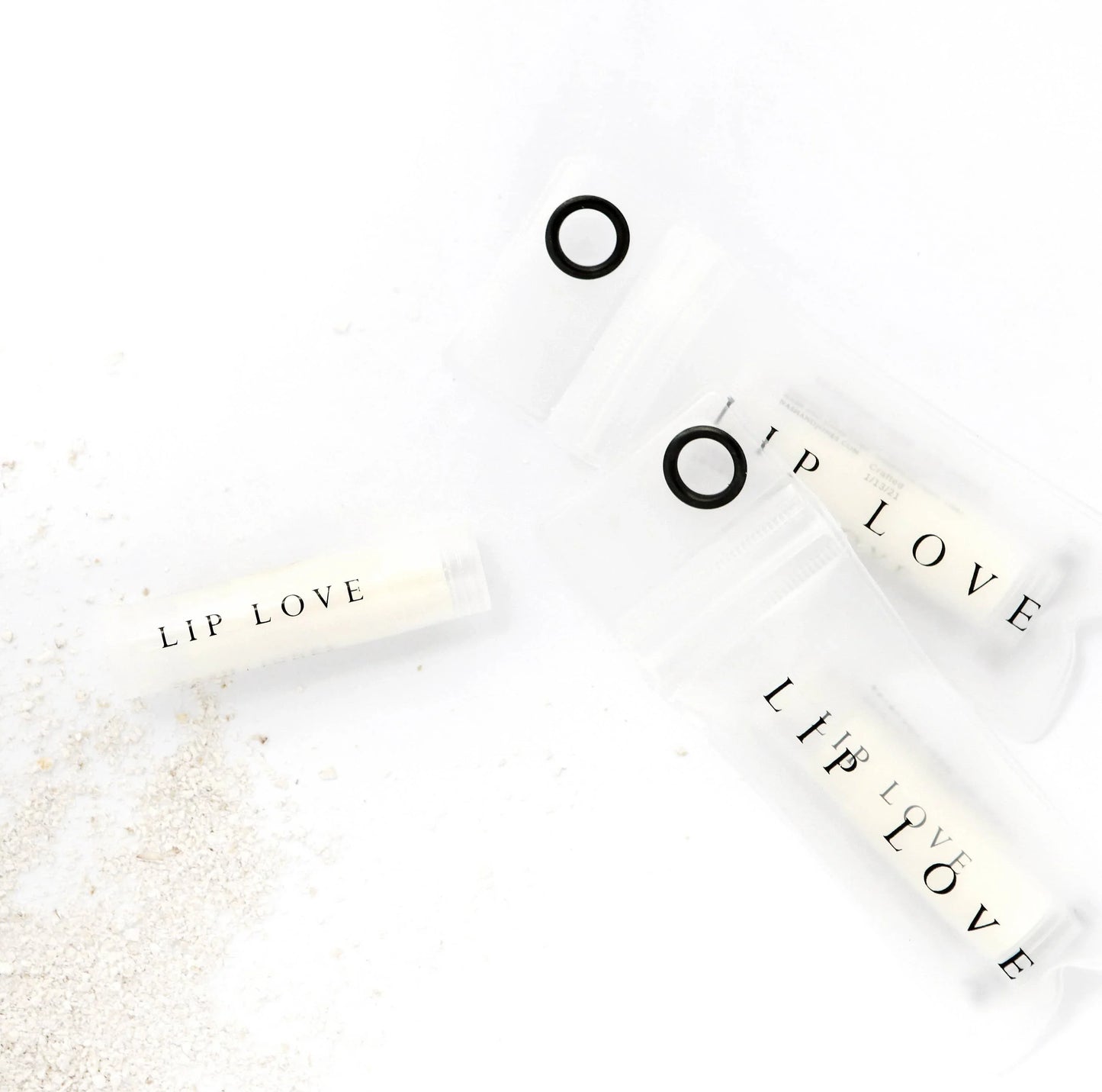 Lip Love chapstick tubes on white surface with sand, minimalist skincare branding. Come see us at Awaken, Franklin, Tennessee