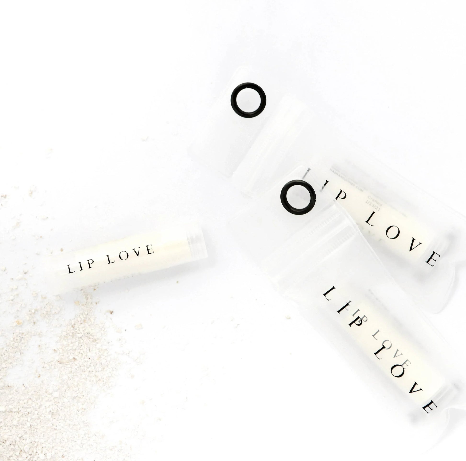 Lip Love chapstick tubes on white surface with sand, minimalist skincare branding. Come see us at Awaken, Franklin, Tennessee