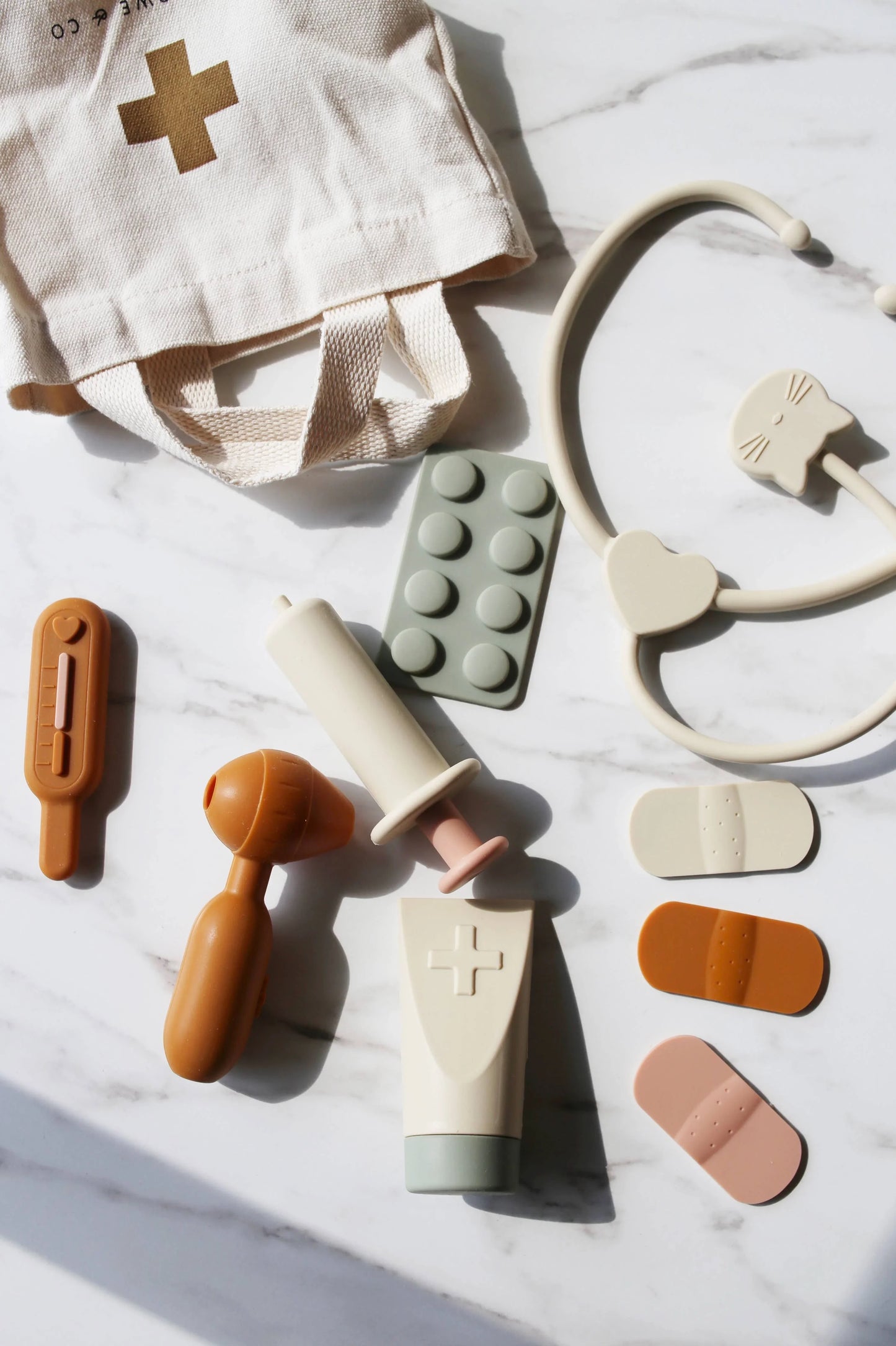 Children's toy medical kit with stethoscope, syringe, thermometer, pills, bandages, and cream on marble table. Come see us at Awaken, Franklin, Tennessee