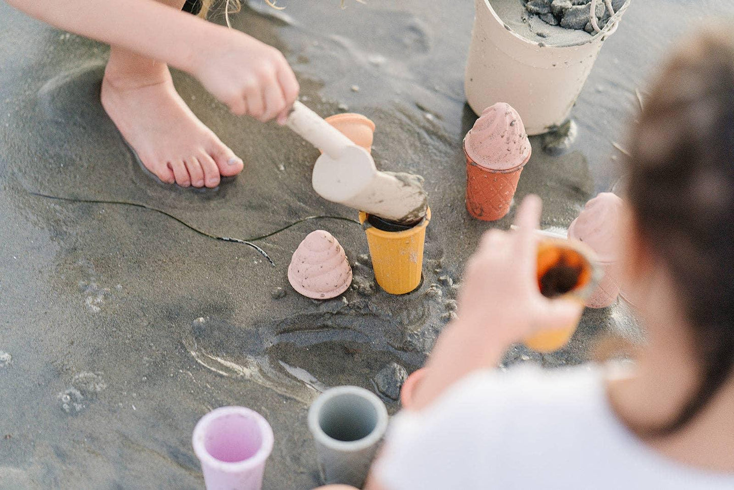 Children playing with plastic cones and buckets on wet sand at the beach. Come see us at Awaken, Franklin, Tennessee