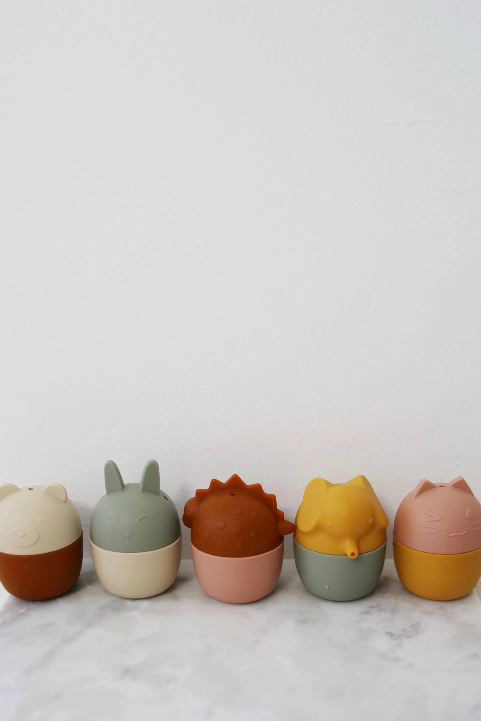 Row of colorful silicone animal-shaped containers on marble surface, minimal background. Come see us at Awaken, Franklin, Tennessee