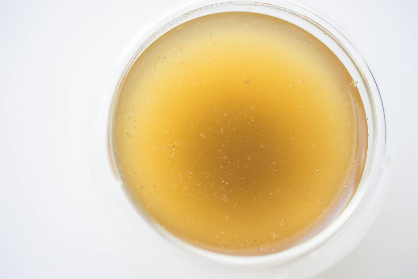 Top view of a glass with amber liquid, possibly broth or juice, on white surface. Come see us at Awaken, Franklin, Tennessee