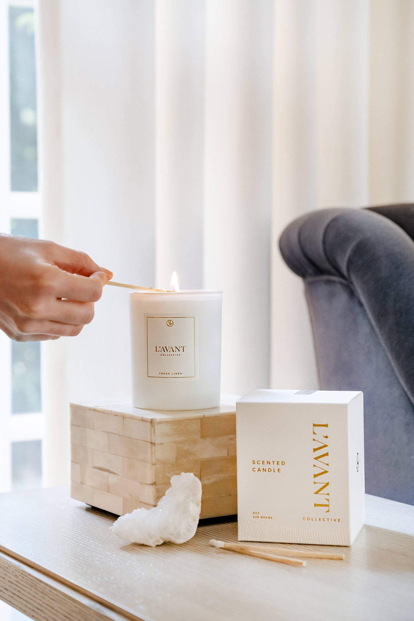 Hand lighting L'AVANT scented candle on table with box, cozy home decor. Come see us at Awaken, Franklin, Tennessee.