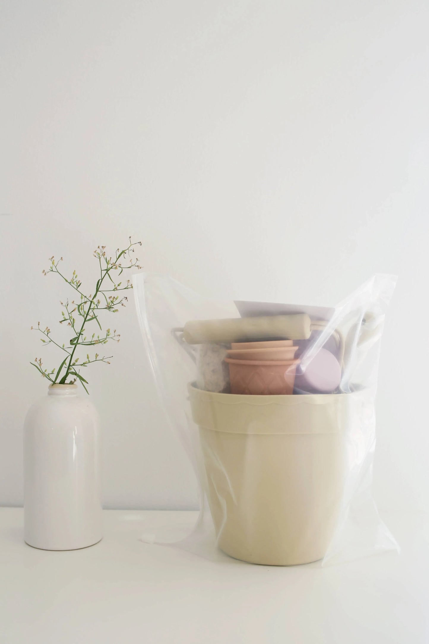 Stacked ceramic planters and gardening tools in clear plastic bag with white vase and sprig nearby. Come see us at Awaken, Franklin, Tennessee