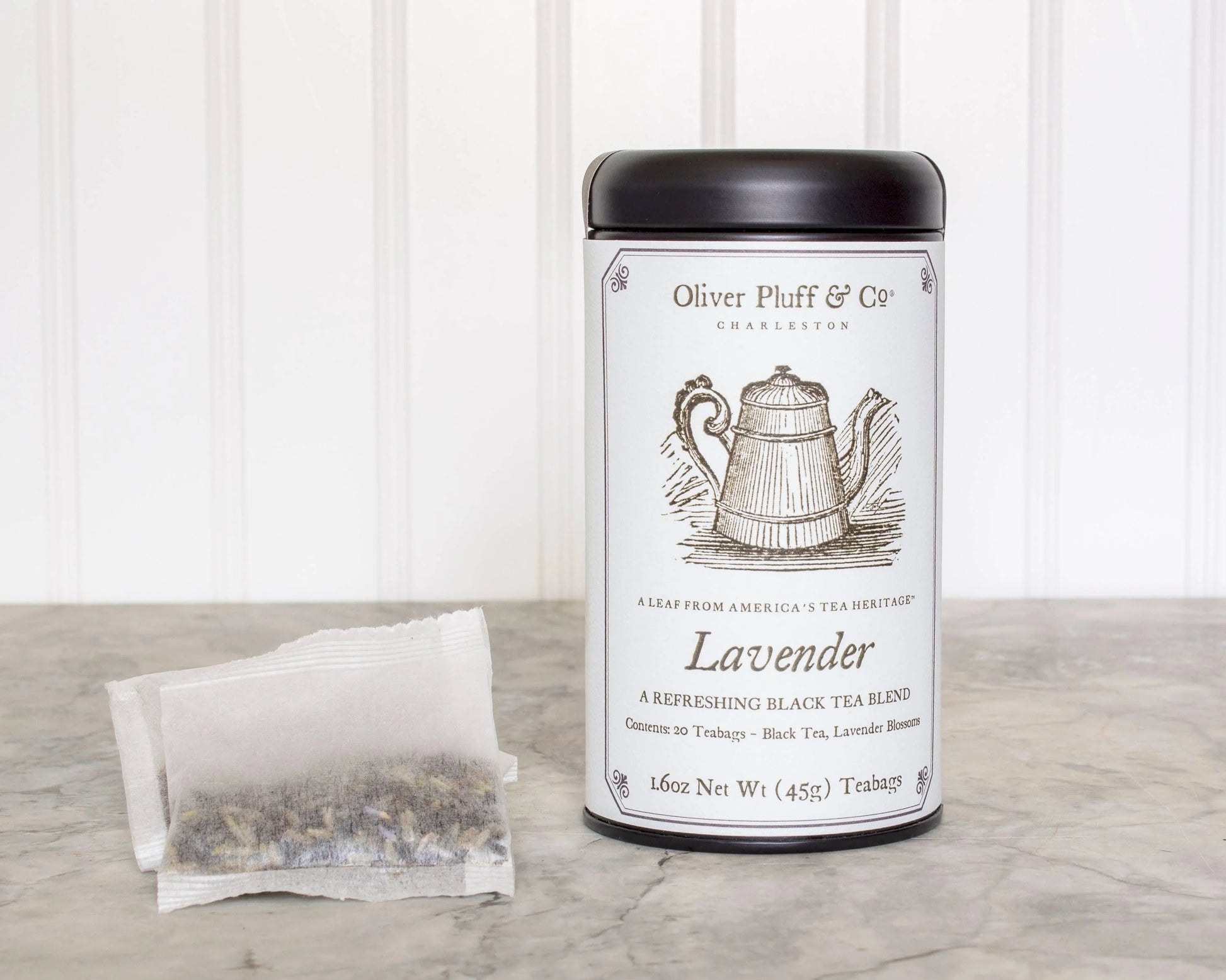 Oliver Pluff & Co. Lavender black tea tin with tea bags on marble surface, white panel background. Come see us at Awaken, Franklin, Tennessee