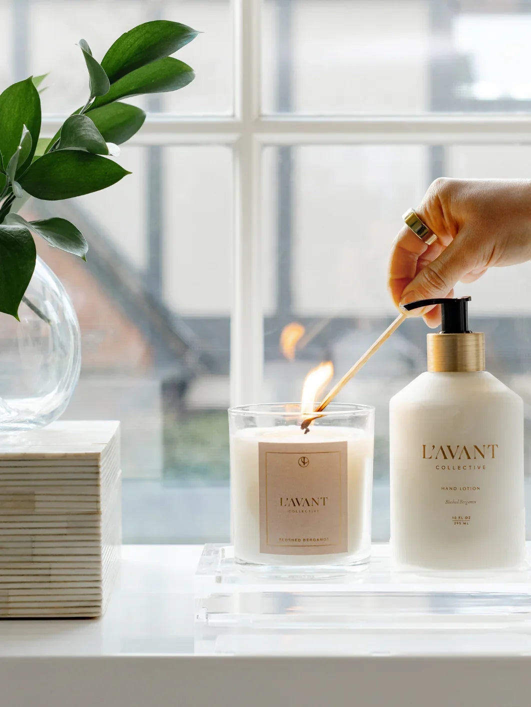 L'AVANT Collective candle being lit beside hand lotion on a windowsill, Come see us at Awaken, Franklin, Tennessee