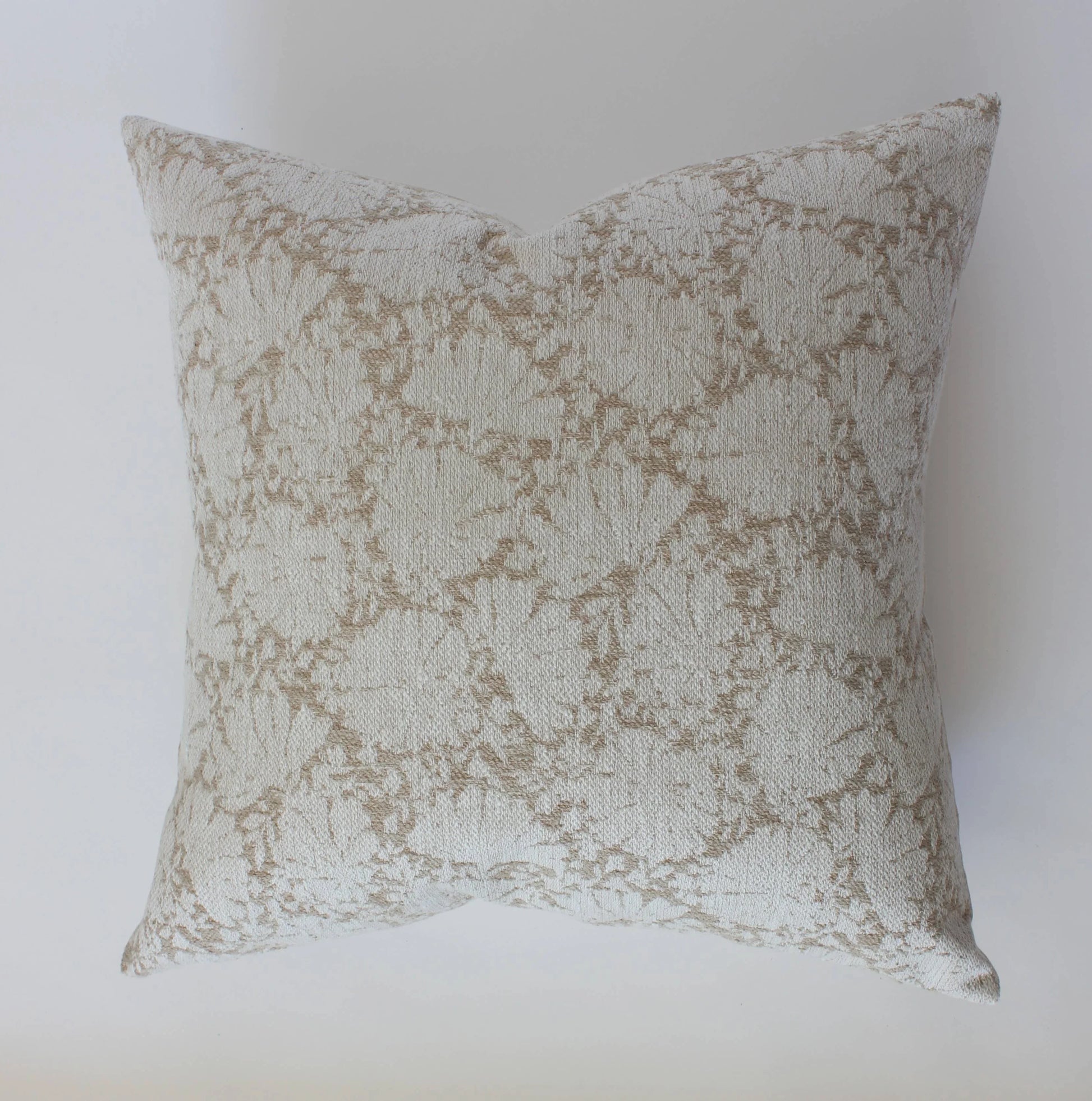 Decorative beige and white textured pillow with floral pattern on white background. Come see us at Awaken, Franklin, Tennessee
